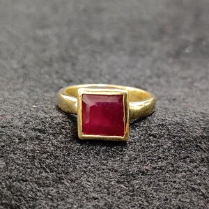 May include: A gold ring with a square-shaped ruby gemstone.