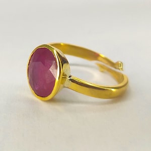 May include: A gold ring with a large, oval-shaped, faceted, pink gemstone.