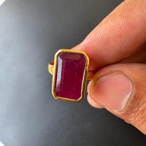 May include: A gold ring with a large, rectangular, dark red gemstone.