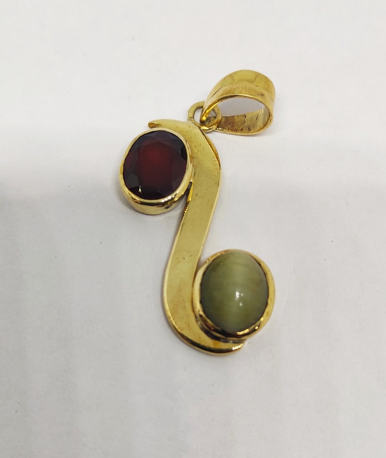 May include: Gold pendant featuring a red and green gemstone. The pendant is shaped like a stylised letter 'S'.