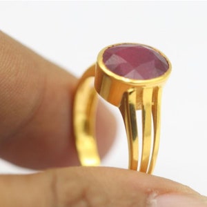 Könnte beinhalten: Ein goldener Ring mit einem großen, ovalen, facettierten, rosafarbenen Edelstein. Der Ring hat eine einfache, dreifach-Krappenfassung und eine Band mit drei vertikalen Linien.