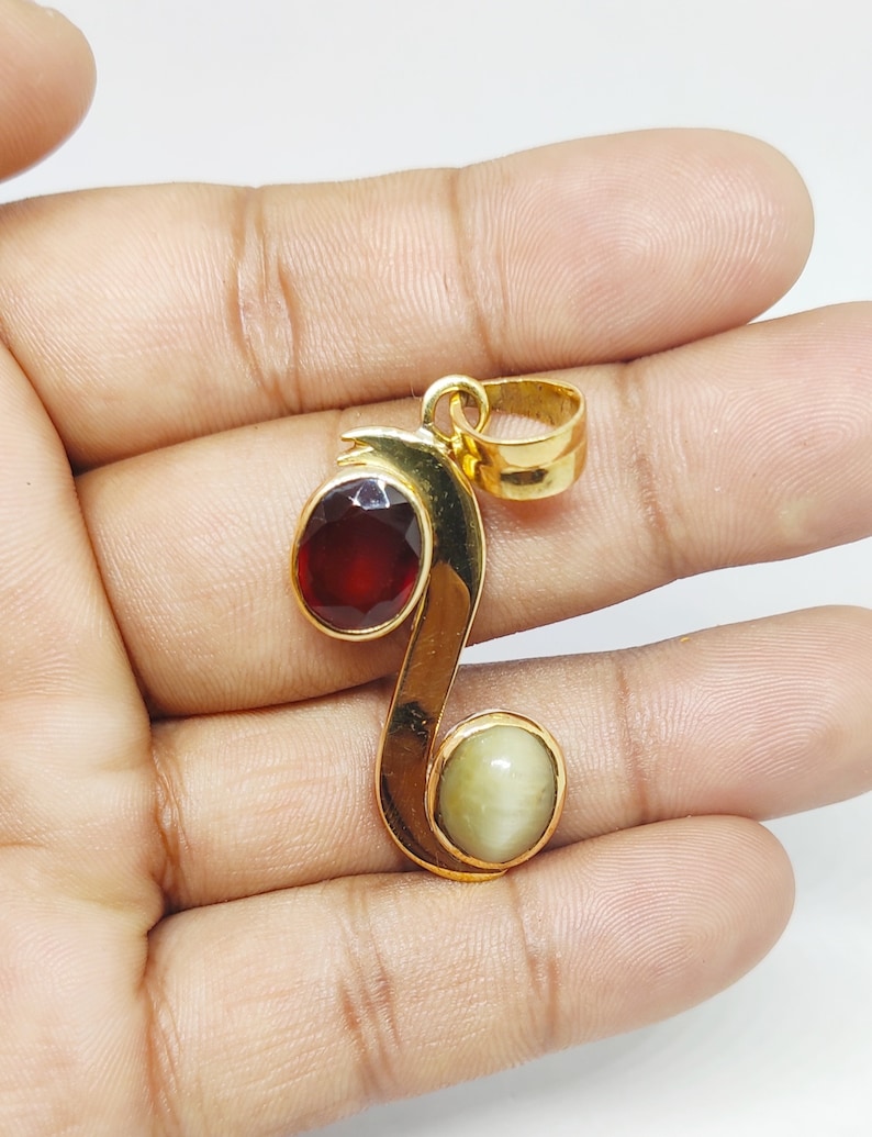 May include: Gold pendant with a red and a white gemstone. The pendant is shaped like a stylized letter S.