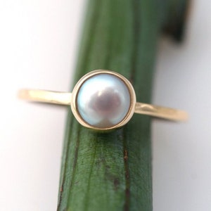 Puede incluir: Un anillo de oro con una perla blanca engastada.