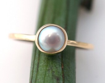 May include: A gold ring with a white pearl set in a bezel setting.