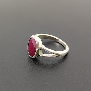 Peut inclure: Une bague en argent avec une pierre ovale rouge foncé sertie dans un sertissage à bélière. La bague a une monture fendue.