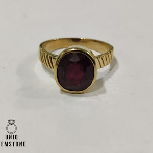 May include: A gold ring with a large, oval, deep red gemstone. The ring band has a textured design. The image also includes the logo "Uniq Gemstone".