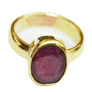May include: A gold ring with a large, oval-shaped ruby gemstone. The ruby is a deep red color and has a slightly textured surface.