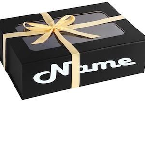 May include: Black gift box with a gold ribbon and a clear window on the top. The box has the word "Name" printed in white on the front.