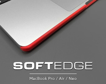 May include: A silver laptop with a bright red protective edge bumper. The text SOFTEDGE is printed below the laptop, followed by the text MacBook Pro / Air / Neo. The laptop features a black keyboard and a smooth metallic palm rest area.