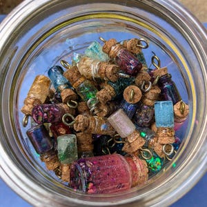 May include: A glass jar filled with small glass bottles with cork tops. The bottles are filled with colourful glitter and iridescent flakes.