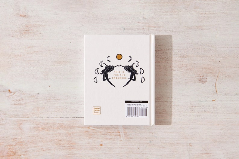 May include: White book cover with a black and gold design. The design features two figures with outstretched arms facing each other. The text "This is for the Dreamers" is printed in gold lettering.