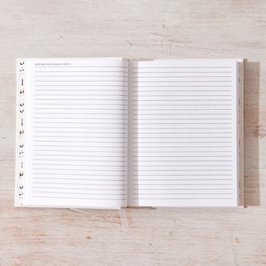 May include: An open notebook with lined pages. The notebook is white with a black spine and a small amount of text on the top left page.