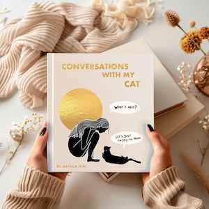 May include: A book titled "Conversations With My Cat" with gold lettering and illustrations. The cover features a woman and a cat, with speech bubbles saying "What's next?" and "Let's just enjoy the meow."
