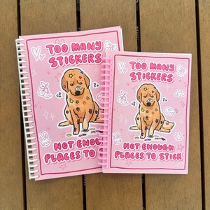 Pink sticker book with cover illustration of a cute golden retreiver dog on a pink background. The dog has lots of stickers stuck on its fur. Text says "Too many sticker, not enough places to stick"