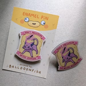 Puede incluir: Dos pines de esmalte con un Espeon Pokémon rosa con un cuchillo sobre su cabeza. Los pines son amarillos y rosas con el texto "Don't Messpeon with Espeon".