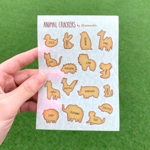 Op de afbeelding: Een vel dierenkoekjesstickers met verschillende dierfiguren, waaronder een eend, konijn, kameel, kat, leeuw, koala, paard, haan, neushoorn en meer. De tekst "ANIMAL CRACKERS" en "by balloonfish" staan bovenaan.