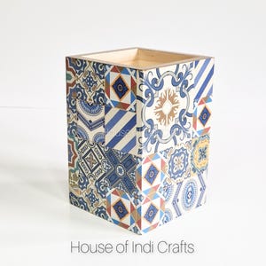 Könnte beinhalten: Eine quadratische Holzkiste mit einem blauen, weißen und gelben Muster. Die Kiste ist aus Holz und hat ein dekoratives Fliesenmuster.