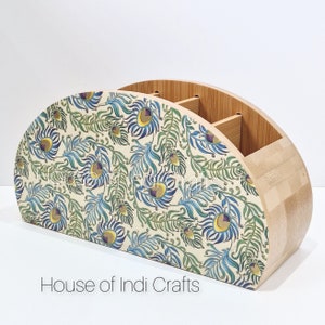 Könnte beinhalten: Ein Schreibtisch-Organizer aus Bambus mit halbkreisförmiger Form. Die Vorderseite hat eine cremefarbene Oberfläche mit einem Pfauenfedermuster in Blau, Grün und Lila. Der Text "House of Indi Crafts" befindet sich unten.