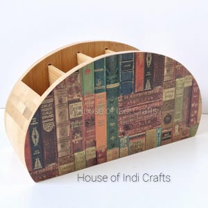 Könnte beinhalten: Ein Schreibtisch-Organizer aus Bambus mit geschwungenem Design. Die Vorderseite zeigt eine Collage von Buchrücken im Vintage-Stil in verschiedenen Farben. Der Organizer hat mehrere Fächer für Stifte, Bleistifte und andere Büroartikel. Der Text "House of Indi Crafts" ist sichtbar.