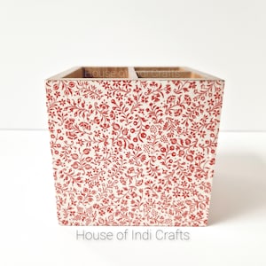 Peut inclure: Un organisateur en bois avec quatre compartiments, orné d'un motif floral rouge et blanc. L'organisateur est étiqueté "House of Indi Crafts".