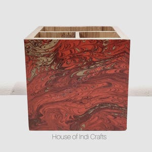 Könnte beinhalten: Ein quadratischer Schreibtisch-Organizer aus Holz mit einem marmorierten rot-goldenen Muster. Die Oberseite hat vier Fächer und ist aus hellem Holz gefertigt. Der Text "House of Indi Crafts" ist unten aufgedruckt.