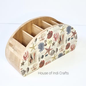 Könnte beinhalten: Ein halbrunder Bambus-Besteckhalter mit vier Fächern. Der Halter ist mit einem Muschel- und Korallendesign verziert. Der Text "House of Indi Crafts" ist auf der Unterseite aufgedruckt.