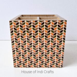 May include: A wooden desk organizer with a leaf pattern in shades of brown, orange, and green. The organizer has multiple compartments and the text "House of Indi Crafts" at the bottom.