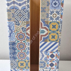 May include: A wooden tissue box featuring a mosaic tile design in blue, white, and yellow. The box is rectangular with a central opening for tissue access. The text "House of Indi Crafts" is displayed on the front.