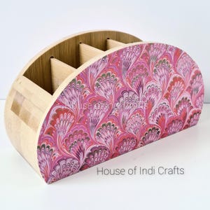 Könnte beinhalten: Ein Holz-Schreibtisch-Organizer mit halbkreisförmiger Form. Die Vorderseite ist mit einem rosa, roten und grünen Marmormuster verziert. Der Organizer hat mehrere Fächer zur Aufbewahrung. Der Text "House of Indi Crafts" ist sichtbar.