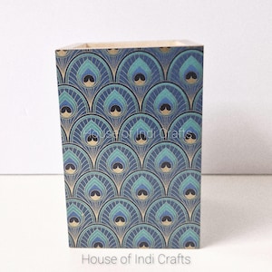 Könnte beinhalten: Ein rechteckiger Stifthalter mit Pfauenfedermuster. Der Halter ist überwiegend marineblau mit türkisfarbenen und goldenen Akzenten. Die Worte "House of Indi Crafts" sind unten aufgedruckt.