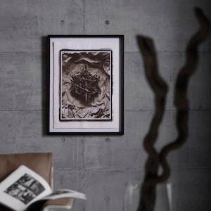 May include: A framed black and white photograph of a cluster of metal objects on crumpled paper. The photograph is hanging on a gray concrete wall.