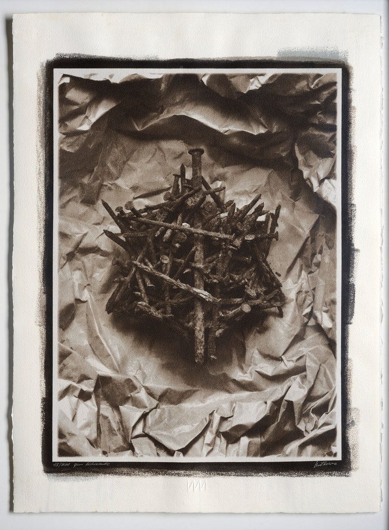 May include: A black and white photograph of a pile of rusty nails arranged in a cross shape on a crumpled piece of brown paper.