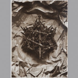 May include: A close-up of a pile of rusty nails arranged in a starburst pattern on a crumpled brown paper background.