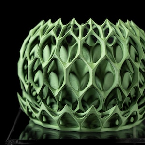 Può includere: Una sfera geometrica verde con un motivo a nido d'ape. La struttura traforata presenta forme esagonali ripetute e bordi appuntiti. La sfera ha una superficie strutturata ed è posta su uno sfondo nero.