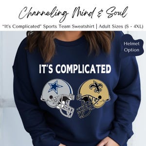 Puede incluir: Sudadera azul marino con la frase "IT'S COMPLICATED" sobre dos cascos de fútbol americano. Un casco es plateado con una estrella azul, el otro es dorado con una flor de lis negra. Disponible en tallas de adulto.