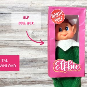 Könnte beinhalten: Druckbare Elfen-Puppenbox-Vorlage. Die Schachtel ist rosa mit einem weißen "Nordpol"-Etikett und dem Text "Elfbie" in weißer und rosa Schrift. Die Schachtel ist für eine kleine Elfenpuppe konzipiert.