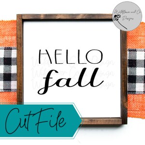 Può includere: Un cartello di legno con sfondo bianco e cornice marrone. Il cartello dice "Hello Fall" in lettere corsive nere. Il cartello è appoggiato su un tessuto a quadri arancio e nero.