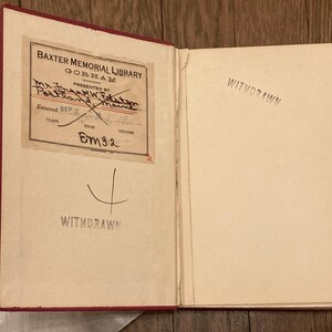 Puede incluir: Un libro abierto con lomo rojo y p&aacute;ginas envejecidas. La p&aacute;gina izquierda presenta una etiqueta de biblioteca con texto, incluyendo "Baxter Memorial Library" y "Withdrawn" estampado debajo. La p&aacute;gina derecha est&aacute; en blanco, tambi&eacute;n estampada con "Withdrawn".