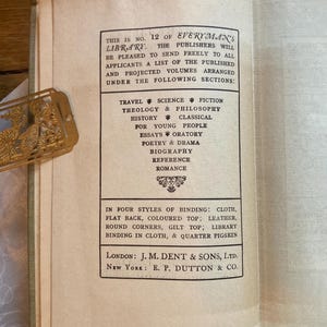 May include: Open book page with text from Everyman's Library, listing sections like Travel, Science Fiction, and History. The text also mentions binding styles such as cloth and leather. A gold-colored bookmark is visible.