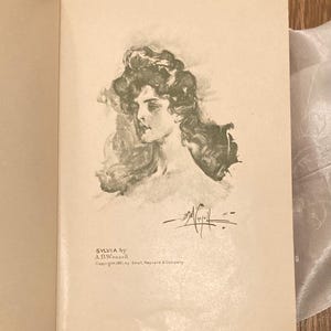 Puede incluir: P&aacute;gina de libro abierta con una ilustraci&oacute;n en blanco y negro de un retrato de mujer. El texto "SYLVIA by A.B. Wenzell" est&aacute; impreso debajo de la imagen, junto con informaci&oacute;n de derechos de autor.