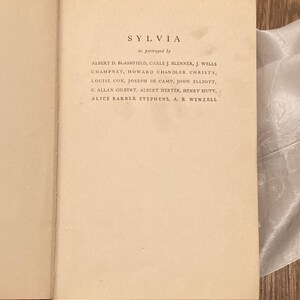 Puede incluir: Libro abierto con el t&iacute;tulo "SYLVIA" y una lista de nombres. El texto est&aacute; impreso en tinta negra sobre papel crema envejecido. La fuente es una fuente serif.
