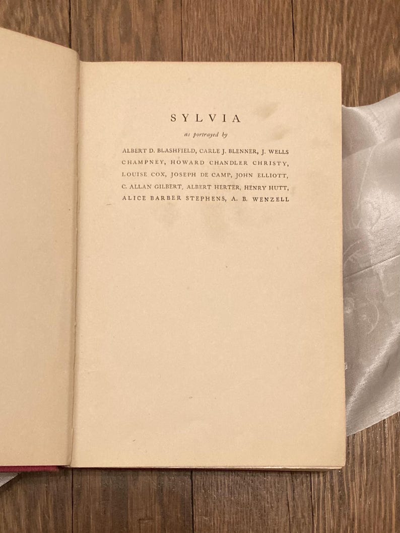 Puede incluir: Libro abierto con el t&iacute;tulo "SYLVIA" y una lista de nombres. El texto est&aacute; impreso en tinta negra sobre papel crema envejecido. La fuente es una fuente serif.