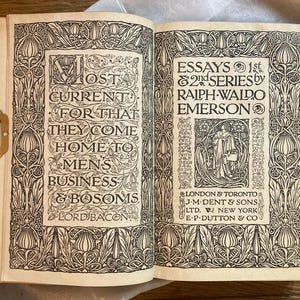 May include: Open book with decorative black and white illustrations and text. The left page reads "MOST CURRENT FOR THAT THEY COME HOME TO MENS BUSINESS & BOSOMS LORD BACON." The right page reads "ESSAYS 1st & 2nd SERIES by RALPH WALDO EMERSON."