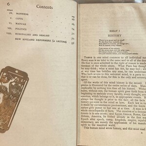 May include: Open book with text and a decorative gold bookmark. The bookmark features an ornate design with figures and a rectangular shape. The book's pages display text from an essay titled "History".