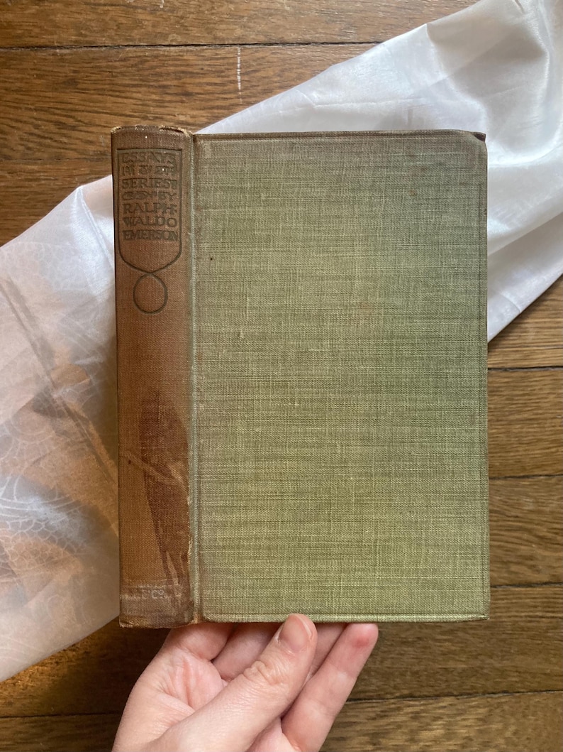 May include: Vintage book with a brown spine and a faded green cover. The spine features the title "Essays in First Series" by Ralph Waldo Emerson. The book is in good condition, with slight wear on the edges.