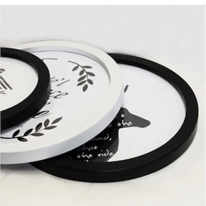 May include: A stack of round picture frames in black and white. The frames have a minimalist design with botanical and animal illustrations. The frames are in varying sizes, with a black frame in the foreground.