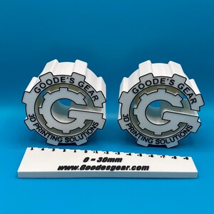May include: Two white 3D printed gears with the logo "Goode's Gear 3D Printing Solutions" and a white ruler with the text "0 = 30mm www.goodesgear.com".