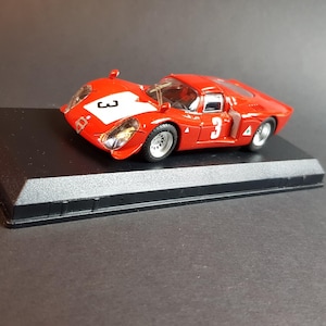 May include: A red toy race car with the number 3 on the side and hood, displayed on a black rectangular base. The car has a white stripe on the hood and is a miniature replica.