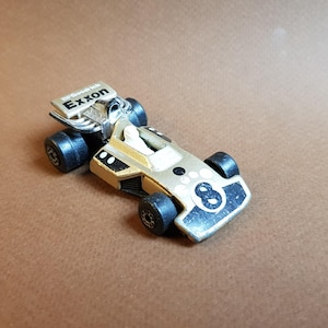 May include: A vintage toy race car in gold and black, featuring the Exxon logo and the number 8. The toy car has black wheels and a detailed design, capturing the essence of classic racing vehicles.