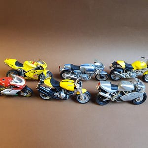 Peut inclure: Collection de sept modèles réduits de motos de différentes couleurs, dont rouge, jaune, argent et bleu. Les motos sont disposées sur une surface marron, mettant en valeur leurs détails. L'image met en évidence la diversité des modèles.